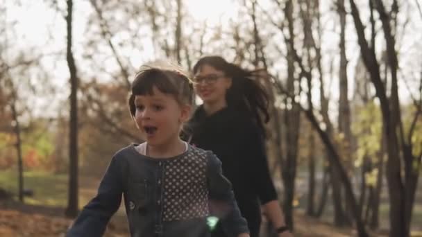 母女俩在秋天的公园里跑步 家庭在秋天公园以慢动作玩乐 幸福的家庭理念 中等镜头 — 图库视频影像