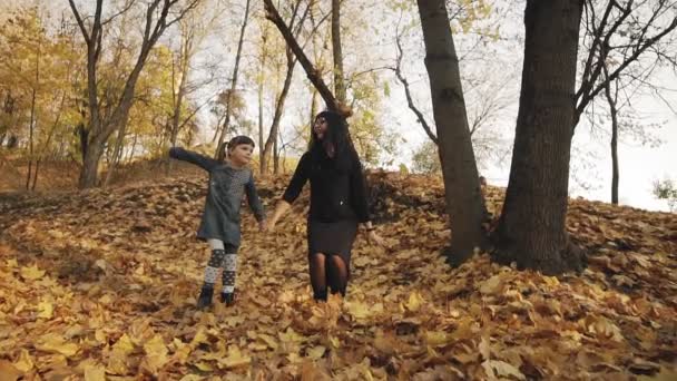 幼い母親と幸せな娘が一緒に秋の公園にジャンプします 彼らは笑って屋外で手を握って楽しんでいます スローモーションで撮影された全長 — ストック動画