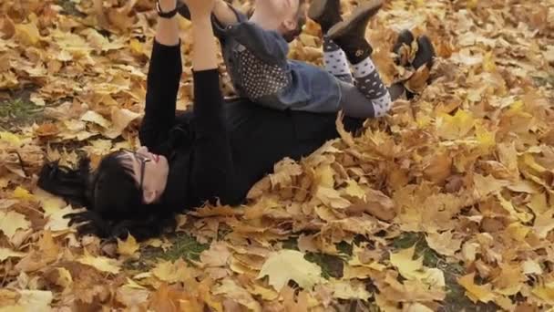 秋の葉の上に横たわっている娘を持つ美しい母 若い母と娘はスローモーションで秋の公園で楽しんでいます — ストック動画