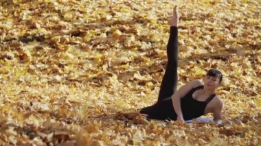 Bacaklarını esneten genç ve çekici bir kız. Parktaki sarı yapraklar üzerinde antrenman yapan bir kadın. Sportif bir kadın spor yapmak için vücudunu esnetir. Spor konsepti. Kopyalama alanı ile tam uzunlukta çekim