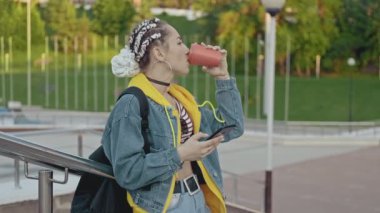 Çekici genç kadın akıllı telefon ile açık havada sohbet ve kahve içme. Çay veya kahve fincan ı ile gülümseyen kız portresi. Copyspace ile yavaş çekimde orta çekim. Kadın kot pantolon