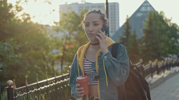 年轻时髦的女人在日落时散步 在电话里说话 快乐的嬉皮士女孩在户外用手机 手里拿着咖啡或茶 生活方式的概念 — 图库视频影像