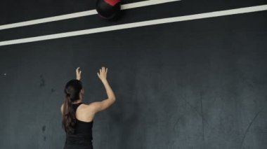 Çapraz formda antrenman yapan genç bir kadın tıp topuyla duvara çarpıyor.