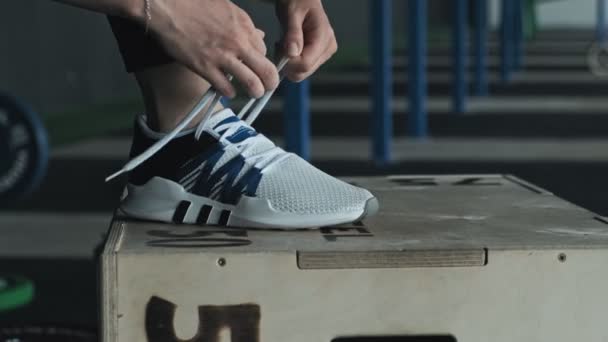 Close-up of feet of female runner getting ready tying running shoes in gym — Stock Video