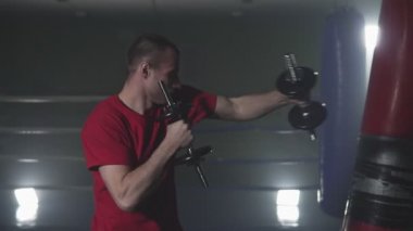 Dumanlı stüdyoda dambıllarla figher eğitimi. Kickboxer eğitim yavaş hareket düşük ışık spor salonunda yumruklar. Koyu arka planda siluet. Ellerde ağırlık