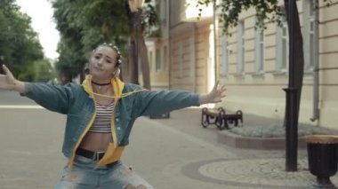 Genç kadın yazın şehrin sokaklarında modern hip hop dansı yapıyor. Dans eden kızı ağır çekimde çekiyoruz. At kuyruklu kot giyen bir kadın.