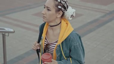 Güneş batarken merdivenlerde yürüyen örgülü, şık bir kadın. Şehir yürüyüşünde elinde kahve olan güzel bir kız. Orta boy. Yaşam tarzı kavramı