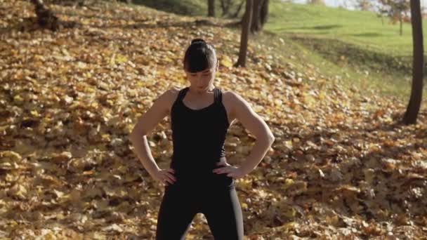 スローモーションで秋の公園で運動する若い女性の肖像画 黒のスポーツウェアで晴れた朝にワークアウト白人女性フィットネスモデル ミディアムショット — ストック動画