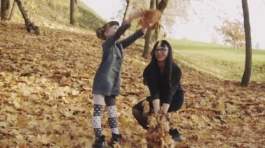 Mutlu genç anne ve küçük kızı autumn parkta oynuyor ve gülüyor. Aile konsepti. Tam uzunlukta çekim