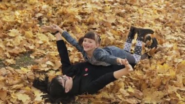 Anne ve kızı yavaş çekimde sonbahar parkında oynarlar. Sonbahar yaprakları açık havada yatan kızı ile mutlu anne