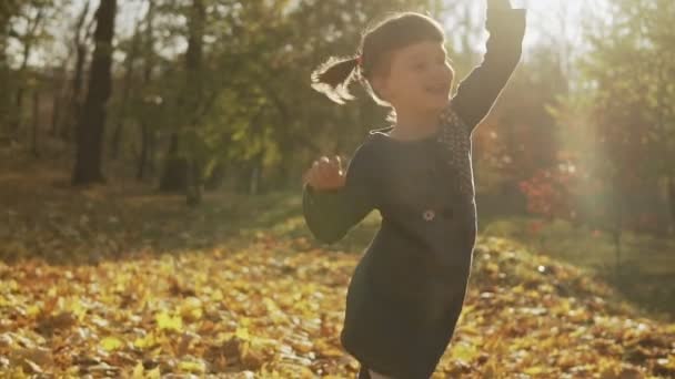 Il tourne en rond dans le parc d'automne au ralenti. Un tir moyen. Bonne fille avoir du plaisir en plein air. Bonheur de l'enfant 