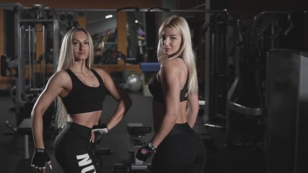 两个健身比基尼金发女孩在黑暗的健身房在慢动作摆姿势 — 图库视频影像