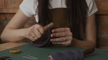 Yavaş hareket aşındırıcı ahşap sopa ile el yapımı deri cüzdan parlatma profesyonel kadın esnaf elleri yakın çekim. El yapımı deri cüzdan üretim süreci.