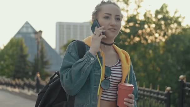 Χαρούμενο χίππη κορίτσι χρησιμοποιώντας το κινητό τηλέφωνο σε εξωτερικούς χώρους με φλιτζάνι καφέ ή τσάι στο χέρι. — Αρχείο Βίντεο