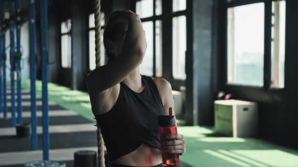 Девушка улыбается со скобками на зубах в спортзале. Портрет женщины с бутылкой воды — стоковое видео
