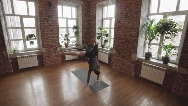 窓の近くで屋内でヨガをしている男手立ちポーズ スタジオでヨガを練習している若者 健康的なライフスタイルのコンセプト — ストック動画