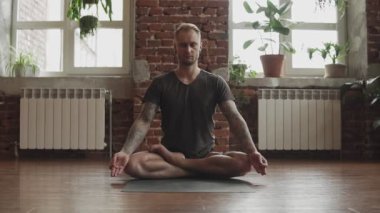 Lotus Yoga yapan yakışıklı adam ahşap zemin ve büyük pencereler ile stüdyoda poz. Özgürlük, sağlık ve Yoga konsepti. Erkek pratik yoga kapalı.