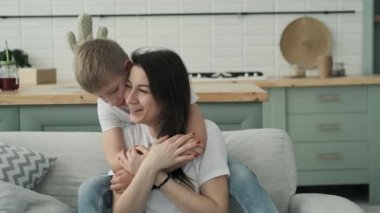 Mutlu genç aile evde birlikte vakit geçirmek. Oğul sarılmak anne yavaş hareket. Oturma odasında gömlek ve kot anne ve oğul