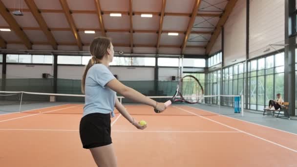 年轻女子用球拍击打网球 女子网球运动员穿着短裤 以慢动作发球 职业网球场上的女孩人们打网球 后视图 — 图库视频影像
