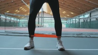 Spor kıyafetin genç kadının düşük açı görünümü bacaklarda elastik bant kullanarak squat ile yan hamle yapıyor. Spor salonunda atletik kadın çömelme yakın çekim.
