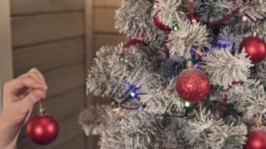 Kız ellerinin kırmızı toplarla süslenen noel ağacını yakın çekimde, genç kadın Noel ağacını süsler. Yavaş çekimde Xmas kavramı