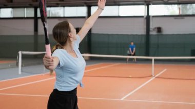 Spor giyim ve uzun saç tenis geniş hizmet topu yapma genç kadın. Bayan tenisçi hizmet orta atış. Yavaş çekimde tenis oynayan gençler