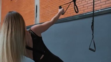 Sporcu genç kadın spor salonunda trx fitness kayışları ile pull up yapıyor. Kapalı mekanda egzersiz yapan fitness kadın yakından görünümü. Spor salonunda eğitim