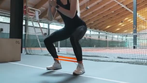 年轻女子锻炼与弹性运动带或带在健身房蹲下 女性锻炼与橡胶弹性带在慢动作 相机幻灯片 — 图库视频影像