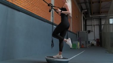 Atlet kadın spor salonunda trx fitness kayışları ile çömelme. Slayt kamerası. Genç kadın yavaş çekimde Trx egzersiz yapmak