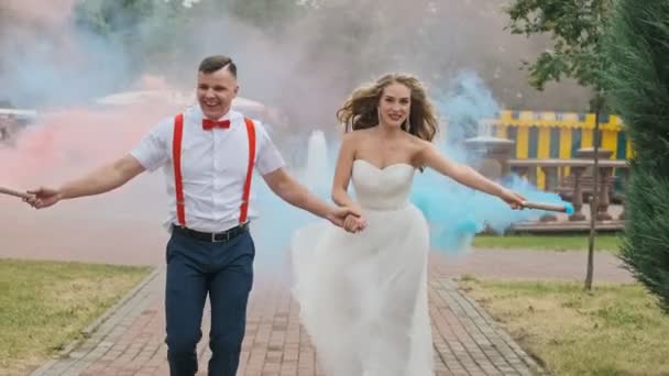 快乐的新娘和新郎在公园里挥舞着红色和蓝色的烟雾 新婚夫妇在户外散步 微笑和玩乐 — 图库视频影像