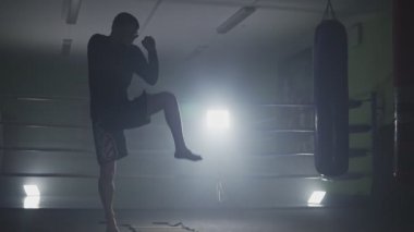Ağır çekimde düşük ışık salonunda eğitim tekme boksör. Muay Tay savaşçı duman. Siluet koyu arka plan üzerinde