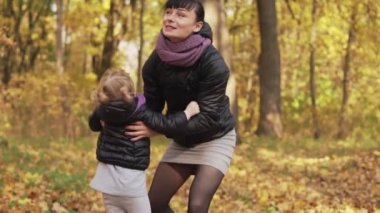 Sonbahar parkında annenin elinde küçük bir kız. Kızı ve genç anne açık havada eğleniyor