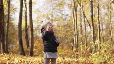 Mutlu küçük kız sonbahar parkında zekâ sabun kabarcıkları oynuyor. Kız yavaş çekimde sabun kabarcıkları yapar