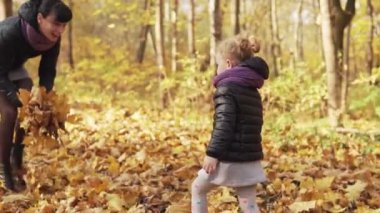 Sevimli küçük kız ve anne sarı düşmüş sonbahar yaprakları atma. Çocuk ve anne parkta birlikte oynuyor