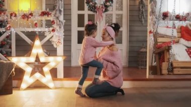 Mutlu anne Noel verandada onun çocuk kızı ile eğleniyor. Anne yavaş çekimde küçük kızını gıdıklıyor. Noel günü pembe pullovers güzel anne ve kızı. Tam uzunlukta çekim
