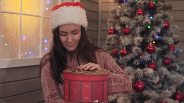 クリスマスの帽子を持つ若い女の子は クリスマス ギフト パッケージを開きます クリスマス コンセプト 祝日と正月 幸せな女の子のクリスマス プレゼントを手に笑顔します — ストック動画
