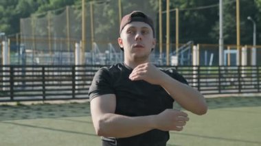 Genç erkek atlet güneşli sabah stadyumda ellerini ve omuzlarını germe. Dışarıda eğitime hazırlanan adam. Sporcunun yakın çekim yavaş hareket sabah egzersiz yapar