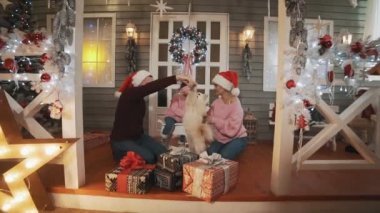 Noel ağacı ve dekor ile verandada oturan küçük kızı ve köpek ile Mutlu aile. Aile konsepti. Noel günü kucaklayan pullovers genç aile. Geniş açı tam uzunlukta çekim