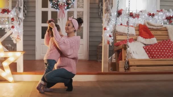 クリスマスの日にピンクのプルオーバーで美しい母と娘 母は小さな娘をスローモーションでくすぐる クリスマスポーチで彼女の子供の娘と楽しんで幸せな母親 フルレングスショット — ストック動画