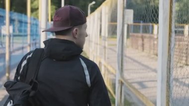 Güneşli sabaheğitim için yürüyen genç adam. Sırt çantası ile kap sporcu geri görünümü. Orta, atış takip edin. Spor konsepti