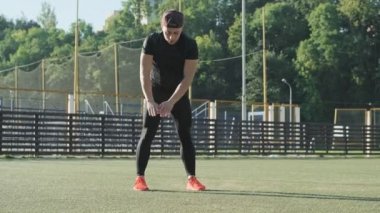 Spor giyimli genç adam antrenmandan önce stadyumda ısınıyor. Güneşli sabahlarda koşmadan önce kasların ısınması. Açık hava sporları. Fitness ve sağlıklı yaşam tarzı kavramı. Tam uzunlukta çekim