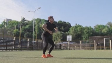 Genç adam açık havada yeşil oyun alanında atlama egzersizleri yok. Spor sırasında güneşli sabah atlama Atletik adam. Yavaş çekim. 4k, Uhd. Geniş açı. Kamera slaytı