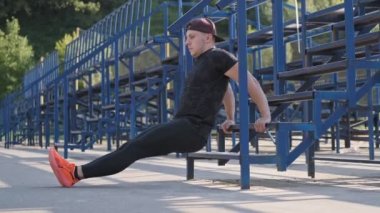 Yakışıklı adam merdivenlerde silah için açık havada egzersiz yapıyor. Açık havada spor ve fitness eğitimi. Şapkalı adam ve turuncu spor ayakkabılar triceps için egzersiz yapıyor. Tam uzunlukta çekim. 4k, Uhd. Yavaş çekim