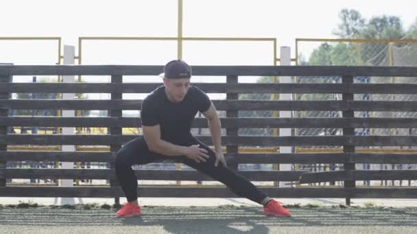 男性穿着橙色鞋子 在阳光明媚的早晨进行体能训练前伸展身体 运动型男子穿着黑色运动服 在慢跑前热身腿部肌肉 全长拍摄 — 图库视频影像