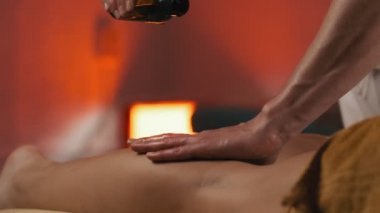 Genç güzel kadın tatil spa salonunda yağ ile bacaklar masaj oluyor. Akşam ışığı. Yakın çekim masaj uzmanı ortam ışığında müşterisine masaj yapıyor. 4k, Uhd