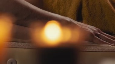 Spa salonunda masaj yaptıran genç kadın. Sırt masajı sırasında dinlenen kadının yakın çekim yavaş harekette masaj masasına yatarak. Mumlu akşam ışığı. 4k, Uhd