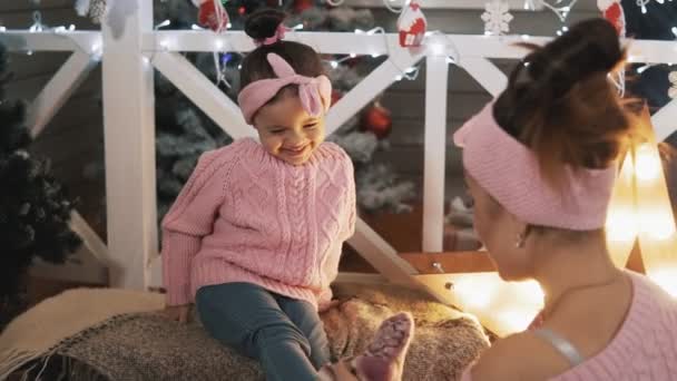 ピンクのプルオーバーで美しい母と娘 クリスマスツリーの近くに彼女の子供の娘と楽しんで幸せな母親 母は小さな娘をスローモーションでくすぐる 母性の概念 ミディアムショット — ストック動画