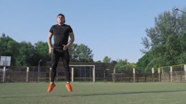 Spor sırasında güneşli sabah atlama Atletik adam. Genç adam açık havada yeşil oyun alanında atlama egzersizleri yok. Yavaş çekim. 4k, Uhd. Geniş açı. Kamera slaytı