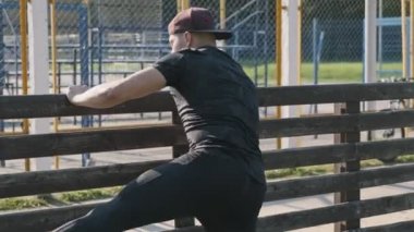 Sportif adam güneşli sabah fitness eğitimi öncesi germe. Siyah spor giyen adam koşudan önce bacak kaslarını ısıtıyor. Turuncu ayakkabılar. Orta atış