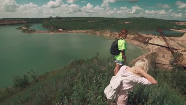 Jolies filles voyageant. Les femelles marchent à la carrière avec le lac. Concept de voyage — Video